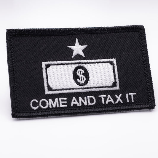 A black patch featuring in white the words "come and tax it" under a outline of a dollar bill, with a star above both.