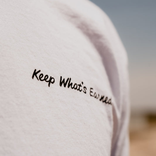A close up photo of the words "Keep What's Earned" in black text on the front left chest of a white